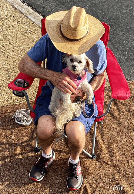 Man sitting in camp chair with little white dog on his lap.